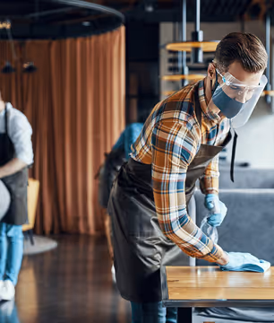 person cleaning a table wearing a mask
